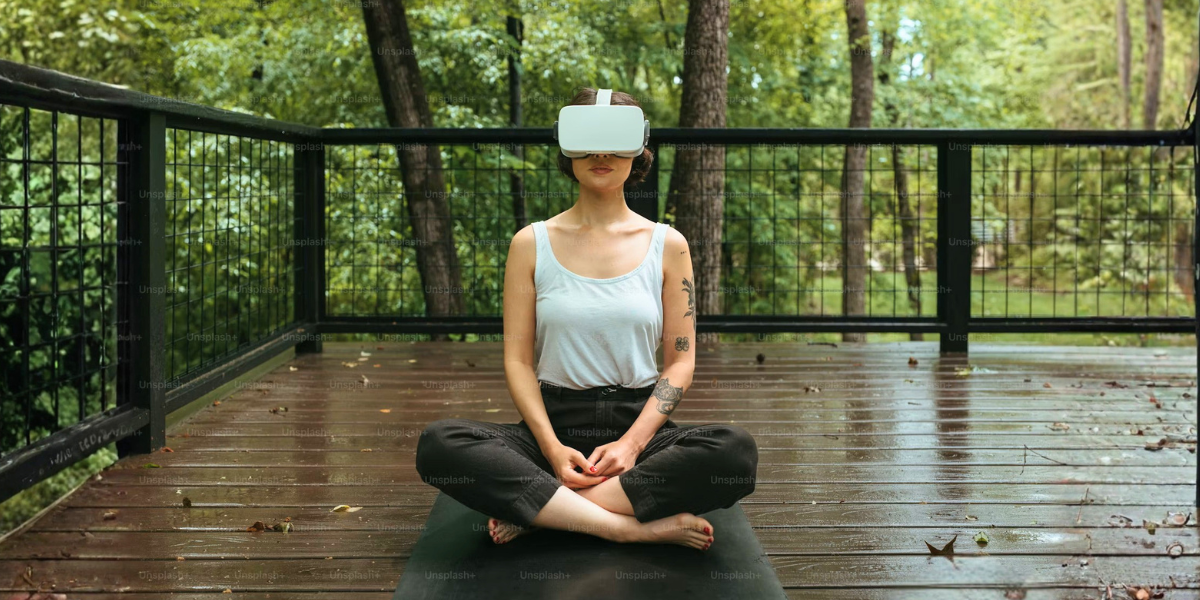 Woman meditating cross-legged outdoors while wearing a virtual reality headset on a wooded deck.