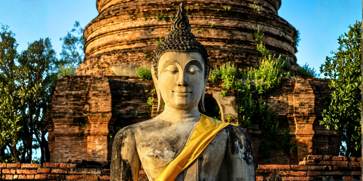 Ancient Buddha statue seated before a brick temple, symbolizing the Buddhist foundations of right mindfulness.